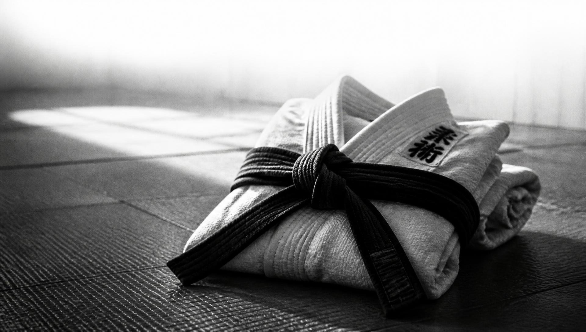 A folded white gi tied with a black belt on dojo mats